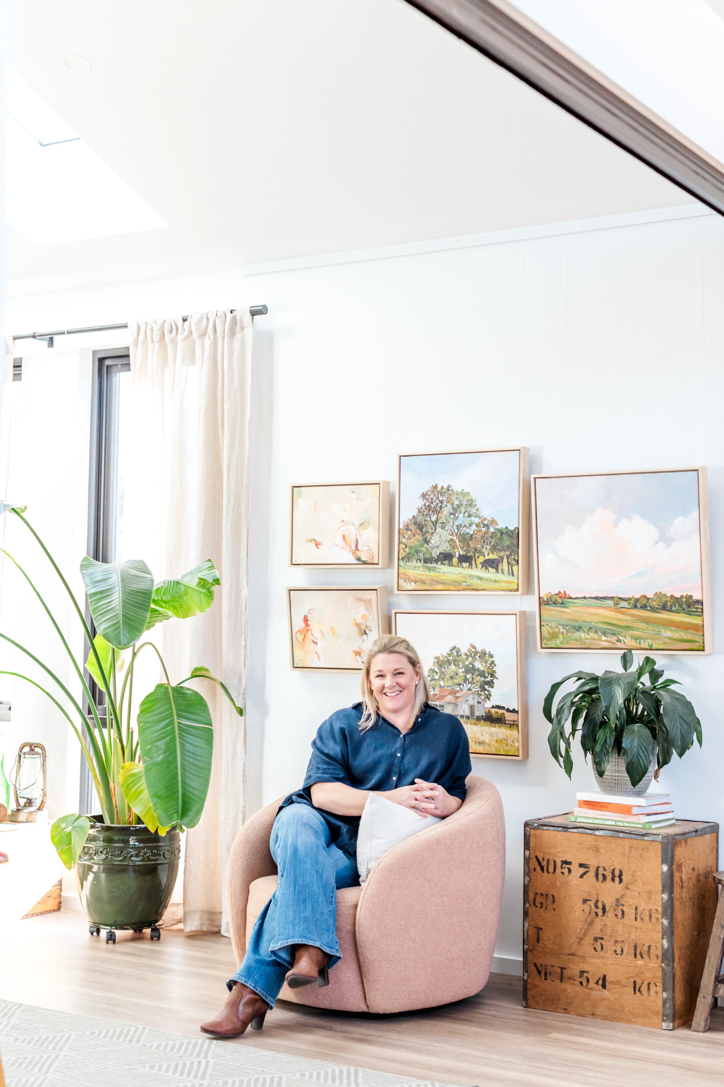 Woman sitting in a pink chair in a bright living room with plants and framed pictures on the wall.
