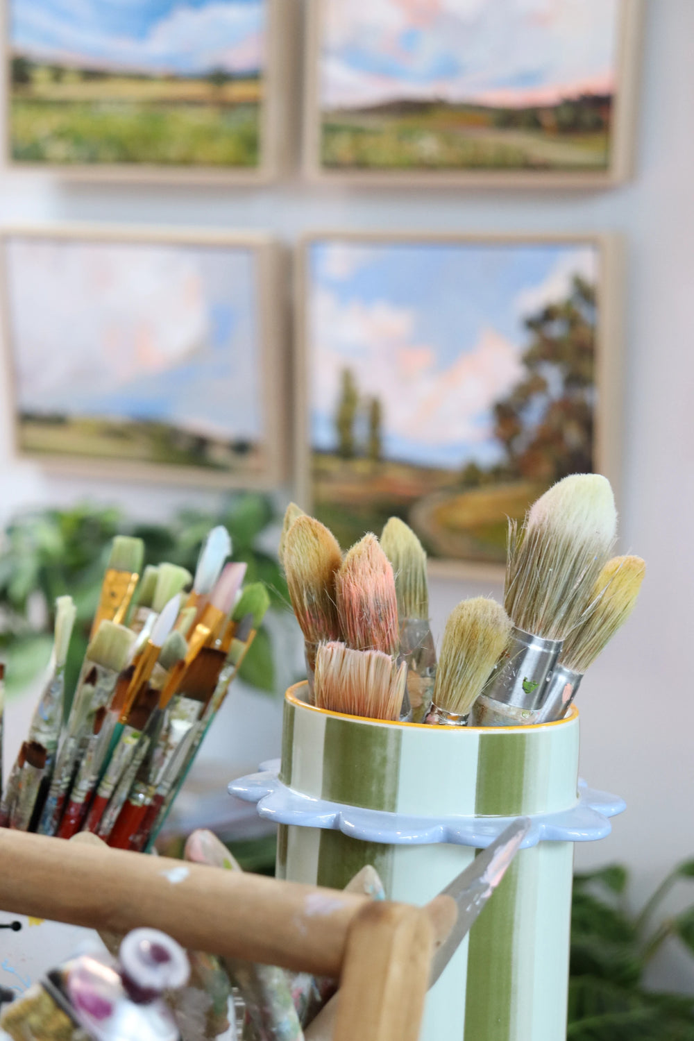 Set of paintbrushes in a holder with scenic paintings in the background